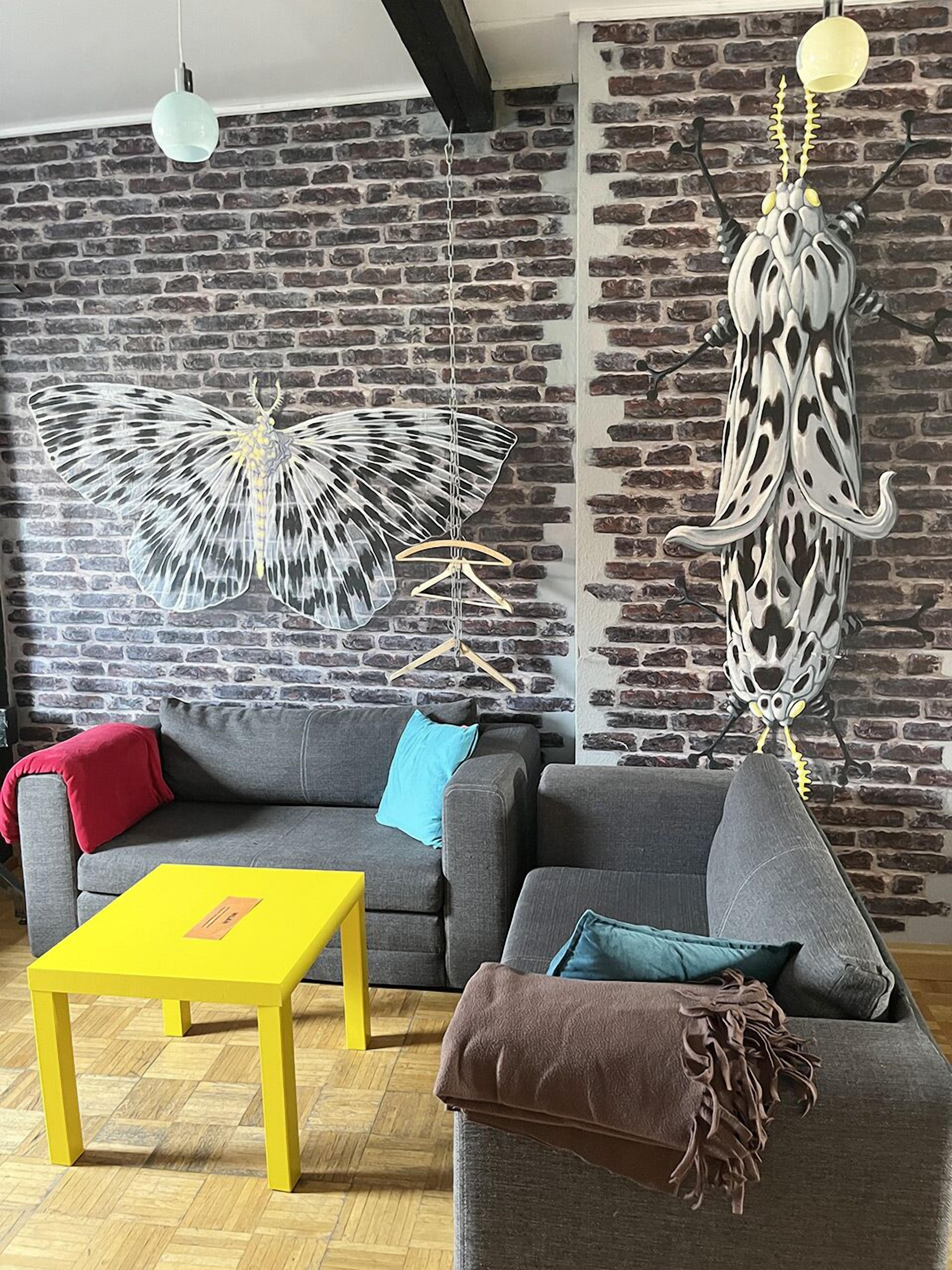 Un salon avec un mur en briques, un canapé, une table jaune et deux éléments de décoration suspendus.