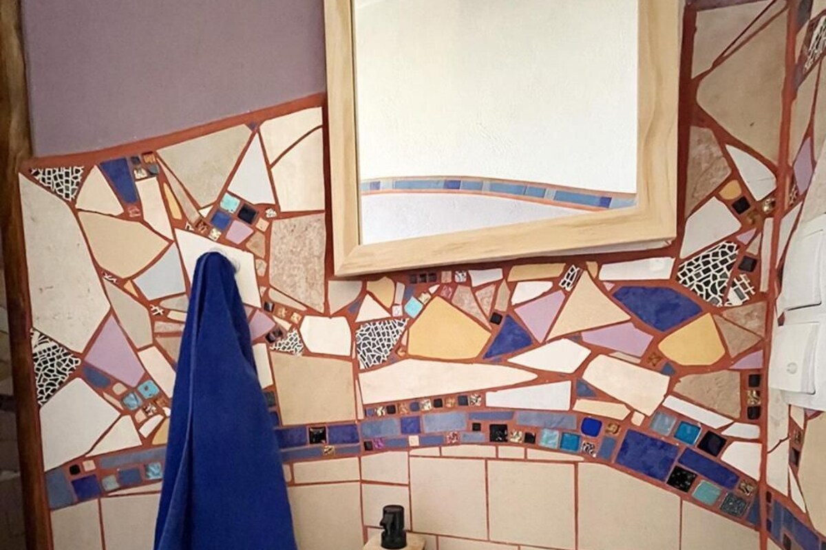 Un bagno con un muro rivestito in mosaico, un lavandino bianco e uno specchio sopra.