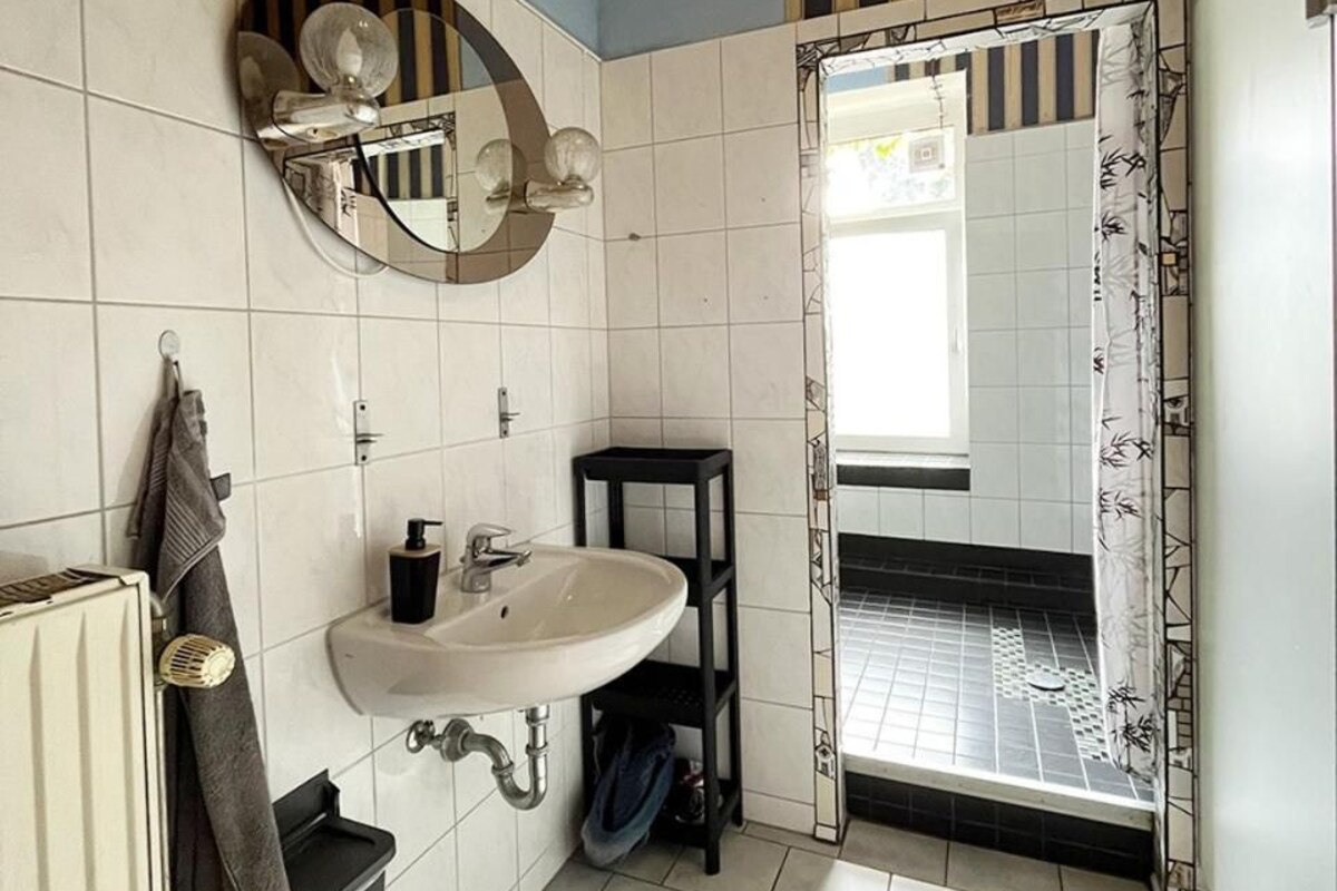 A bathroom with a white sink, a mirror, and a towel rack. There is a window with a view of a tiled floor.