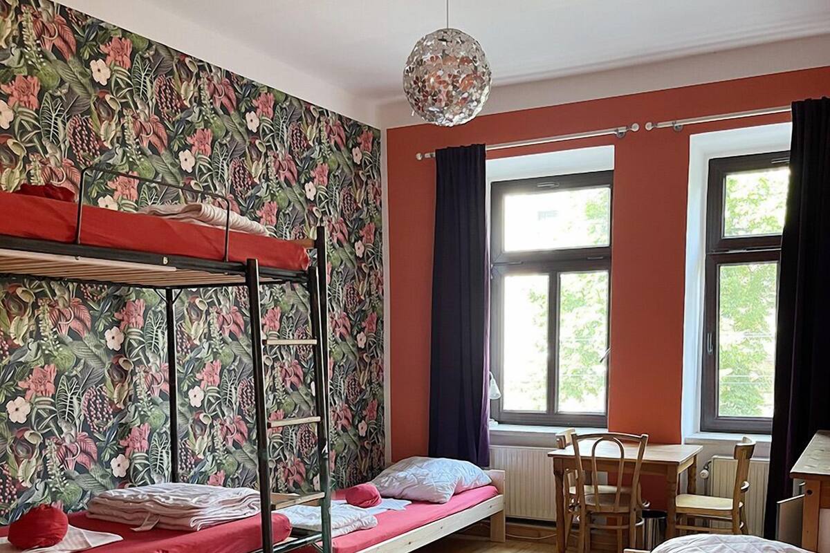 A dormitory room with bunk beds, a desk, and a window with curtains.