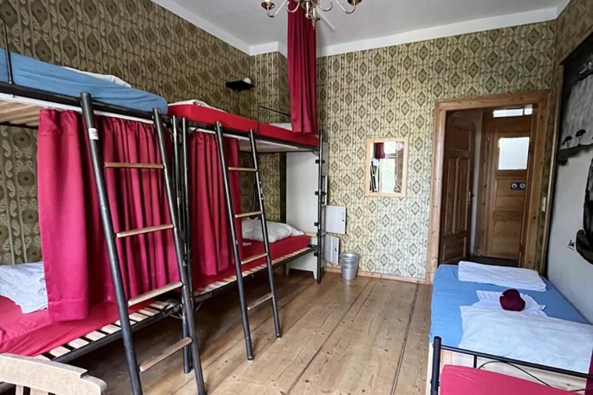 Une chambre de dortoir avec des lits superposés, un lustre, un plancher en bois et un papier peint à motifs.