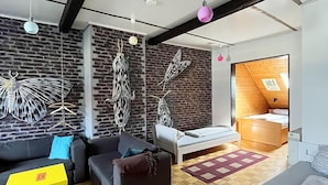 A modern living room with a brick wall, a sofa, a bed, and a wooden floor. - Homeplanet Hostel (Leipzig)