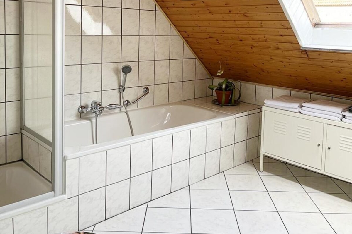 A bathroom with a sloped ceiling, a bathtub, a shower, and a window.