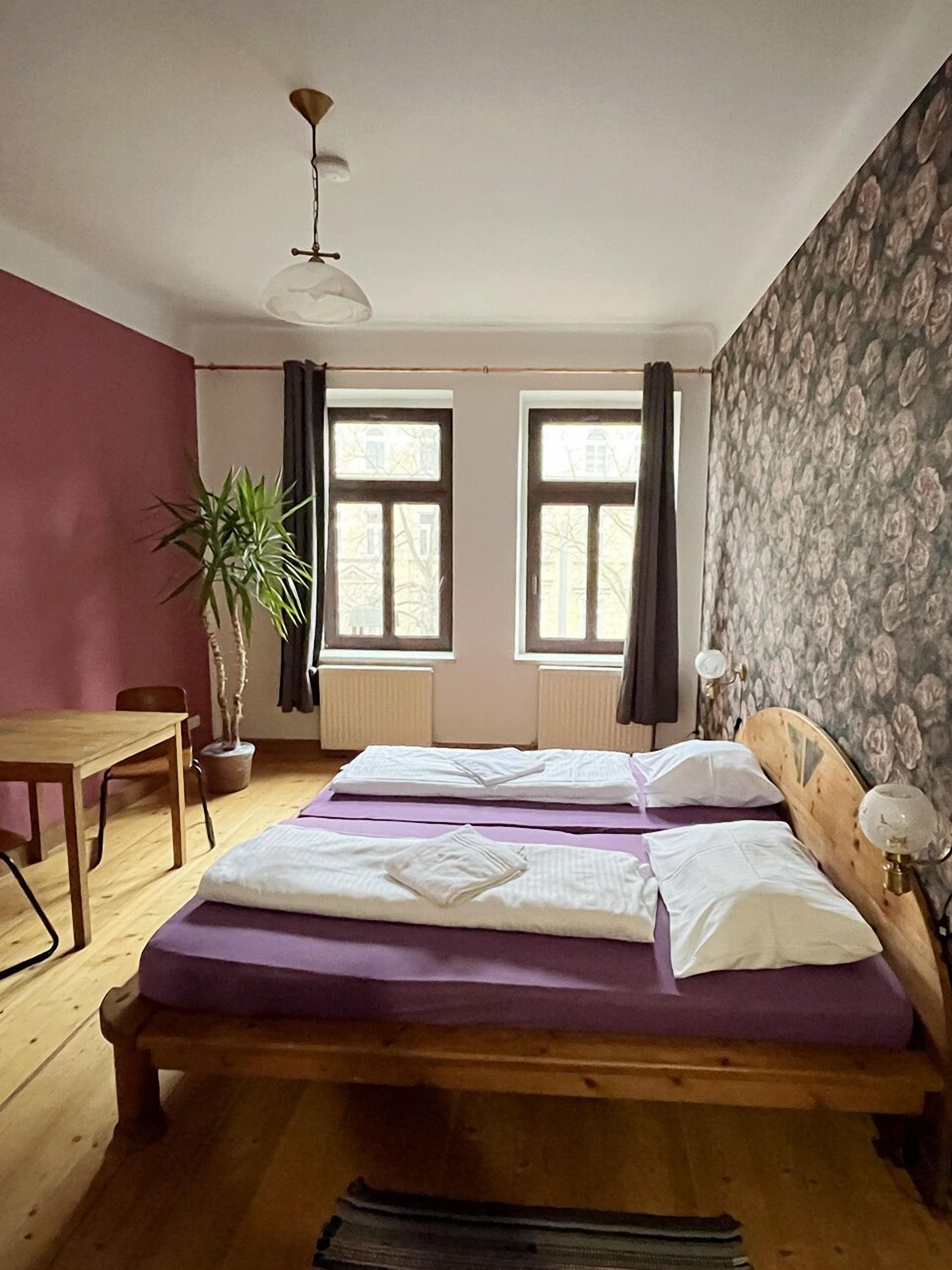 Une chambre à coucher avec un lit en bois, deux fenêtres, un bureau et une plante en pot.