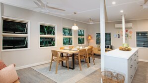 A modern kitchen with a dining area, wooden furniture, and large windows. - The Point. A rainforest and ocean view retreat (Flying Fish Point)