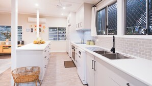 A modern kitchen with white cabinetry, a large island, and a window with a lattice screen. - The Point. A rainforest and ocean view retreat (Flying Fish Point)