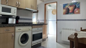 A kitchen with wooden cabinets, a microwave, a toaster, a washing machine, and an oven. - Cozy Apartment in Cudillero (Cudillero)