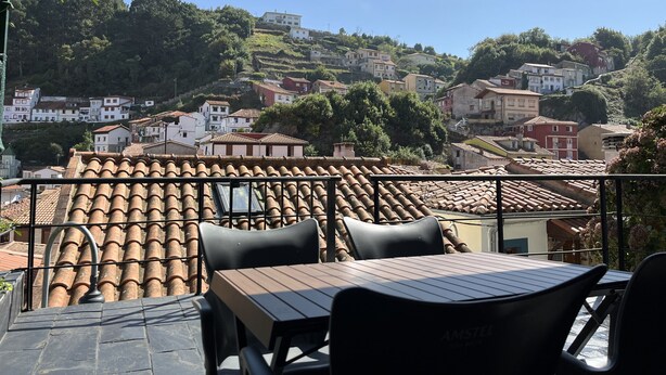 A terrace with a view of a hillside town, featuring terracotta-tiled roofs and a mix of white and red buildings. - Cozy Apartment in Cudillero (Cudillero)