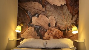 A hotel room with a bed, white pillows, and a wall mural of leaves. There are two wall-mounted lamps on either side of the bed. - Cozy Apartment in Cudillero (Cudillero)