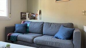 A grey sofa with blue cushions, a small potted plant, and a remote control on a white table. - Cozy Apartment in Cudillero (Cudillero)