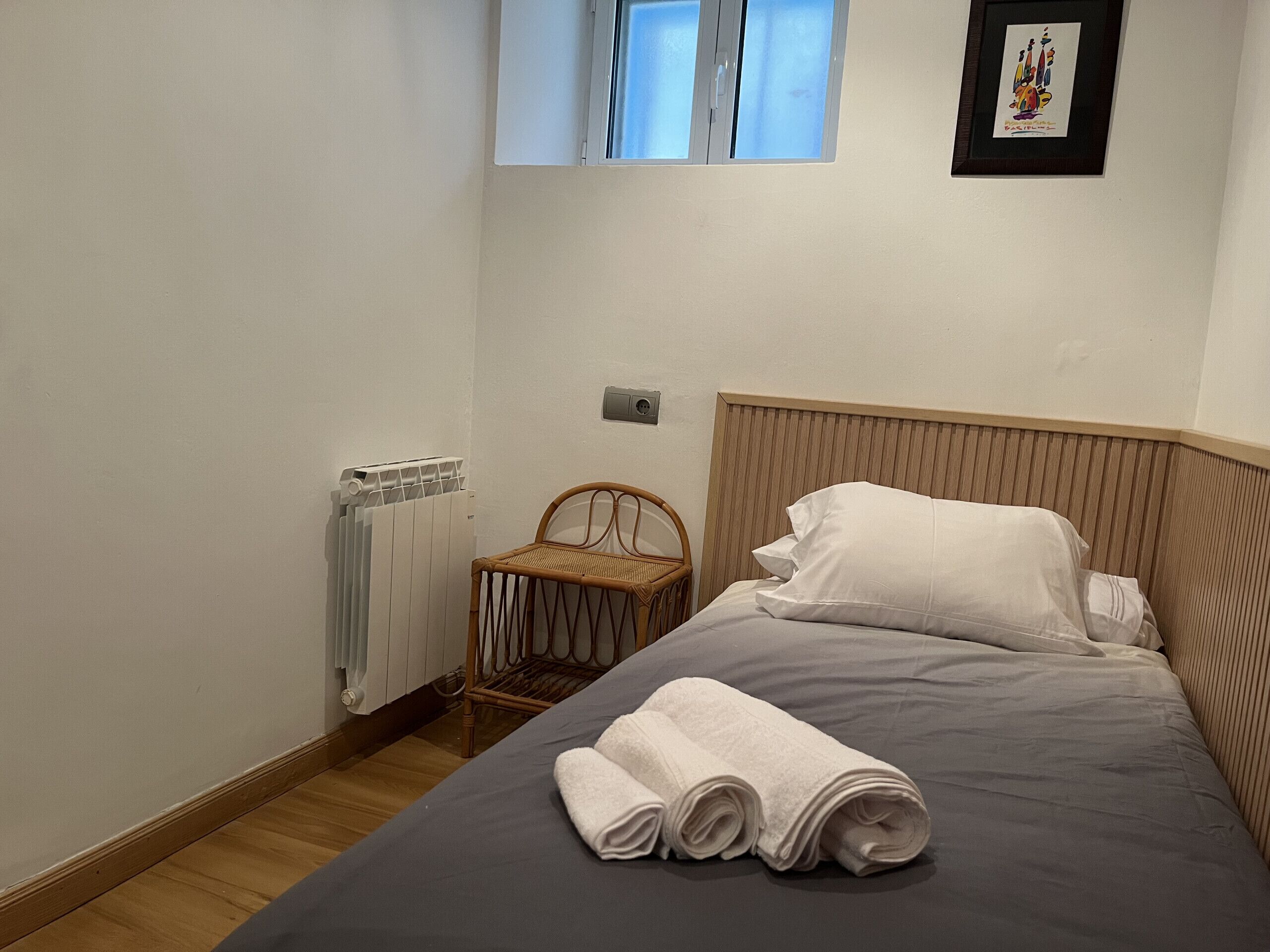 Een slaapkamer met een bed, een radiator, een raam en een ingelijst kunstwerk aan de muur.