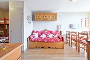 A room with a bunk bed, a wooden cabinet, a sofa with heart-patterned cushions, and a television.