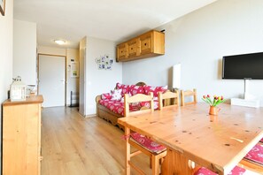 A dining area with a wooden table and chairs, a sofa with red and white patterned cushions, and a wooden cabinet above the sofa. - Apartment for 6 in Saint François Longchamp (1650 m) (Saint-François-Longchamp)