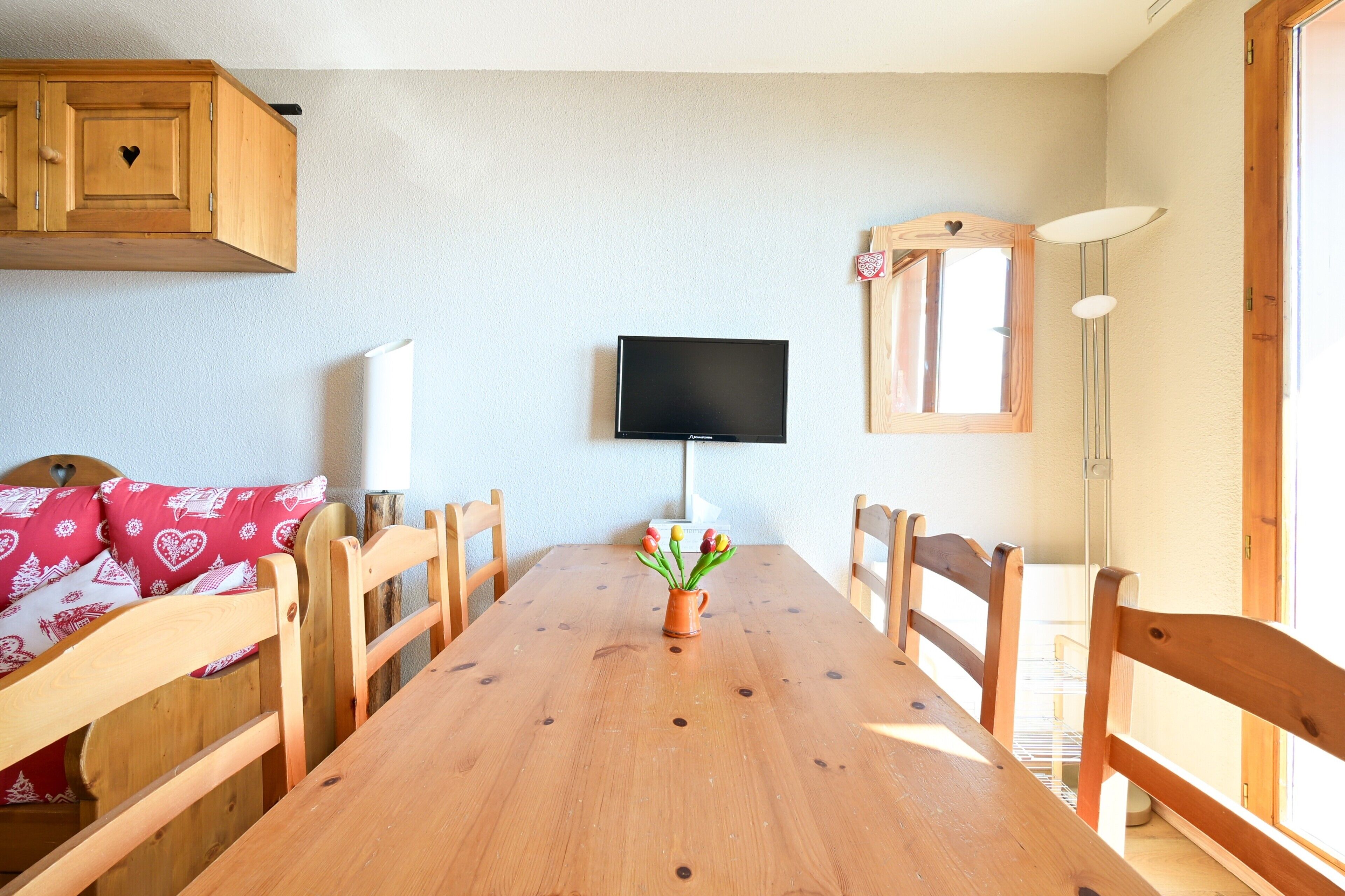 A dining area with a wooden table, chairs, a TV, and a window.