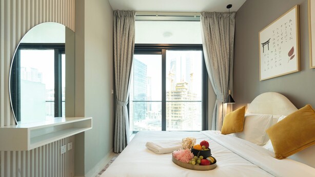 A hotel room with a large bed, a bedside table, a mirror, a window with curtains, and a city view. - Lake-View 1BR Retreat in Business Bay  (Dubai)