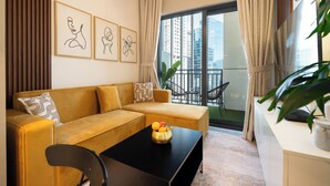 A modern living room with a sofa, a coffee table with fruit, a plant, and framed artwork on the wall. - Lake-View 1BR Retreat in Business Bay  (Dubai)