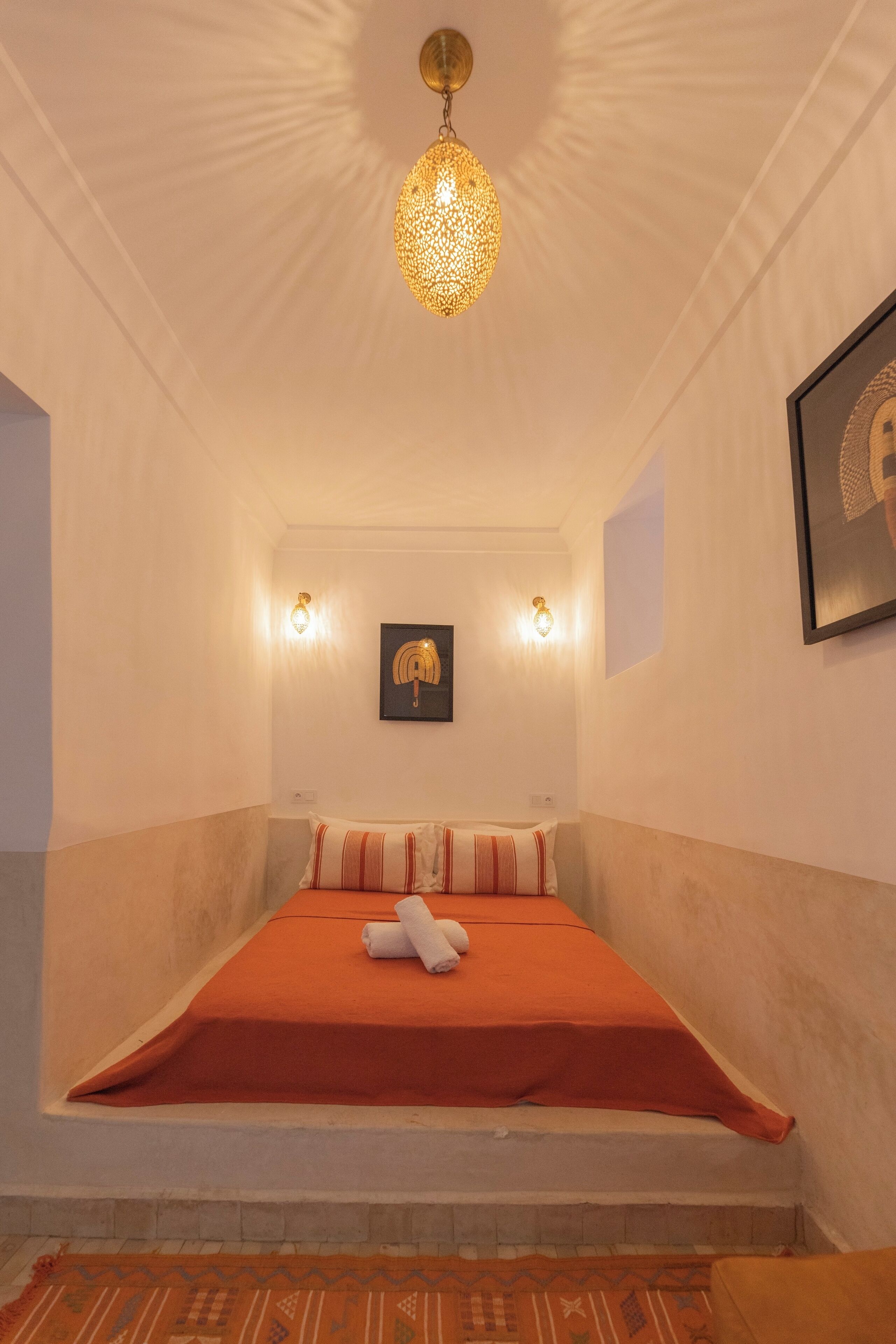 A bedroom with a bed, a patterned rug, and a hanging light fixture.
