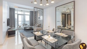 A modern dining area with a glass table, grey upholstered chairs, and a large mirror. - Vogue Damac Prive Walk to Dubai Mall (Dubai)