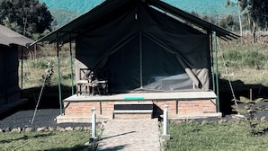 A tented accommodation with a brick base, a table and chairs, and a view of mountains. - Volcanoes Over View Safaris & Camp  (Kinigi)