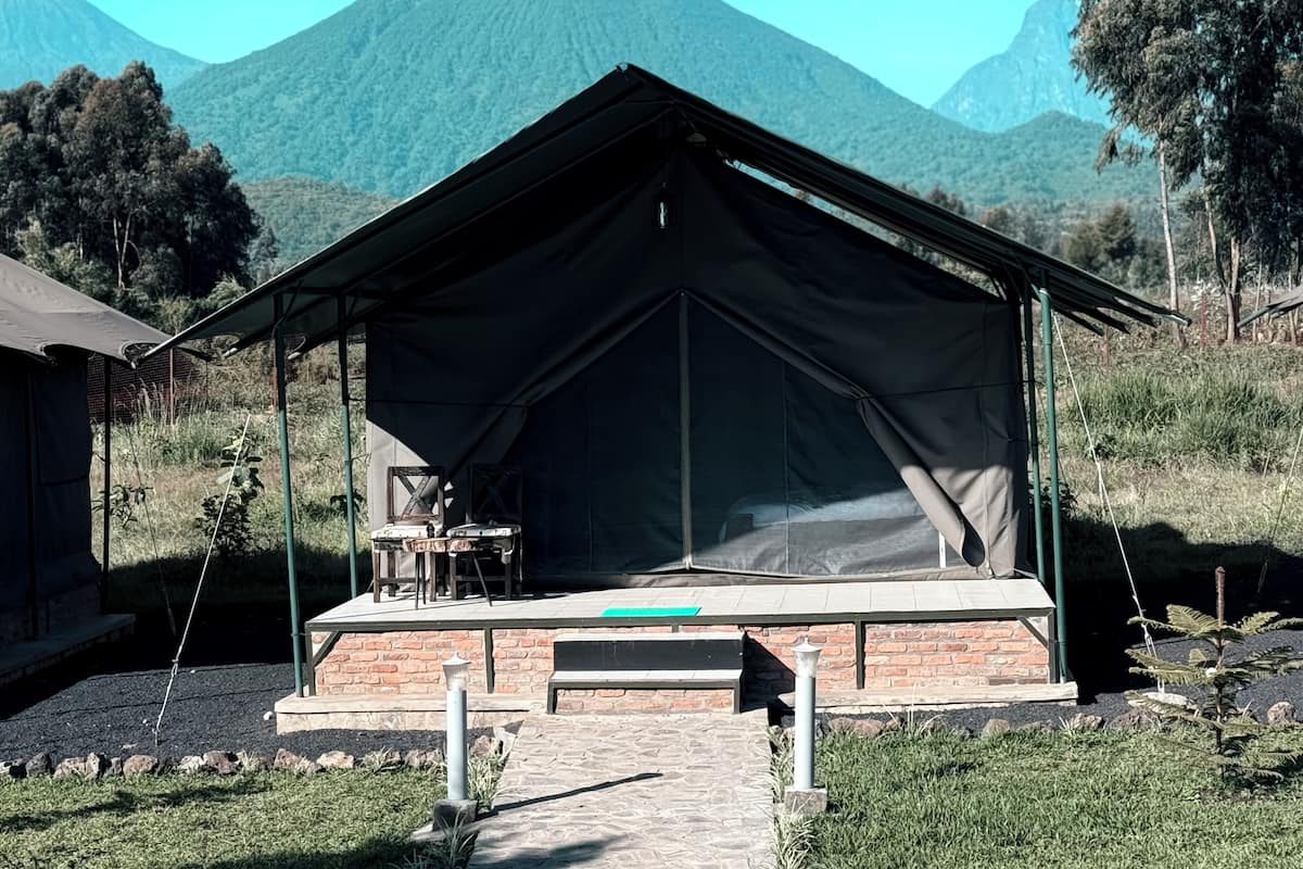 A tented accommodation with a brick base, a table and chairs, and a view of mountains.