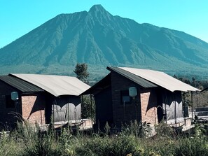 Dos edificios de ladrillo con techos metálicos, probablemente cabañas o pequeñas lodges, frente a una gran montaña.