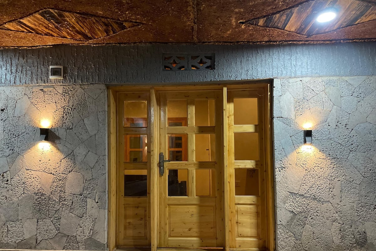 A wooden door with glass panels, flanked by stone walls and two wall-mounted lights.