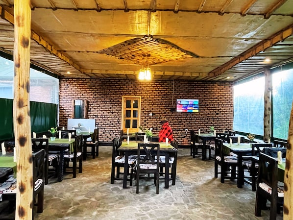 Un restaurante con paredes de ladrillo, mesas y sillas de madera, una pantalla de televisión y un suelo de piedra.