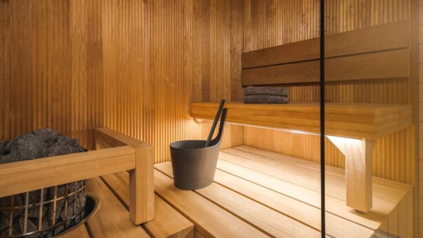 Un sauna avec des bancs en bois, un bassin en pierre et un seau noir.