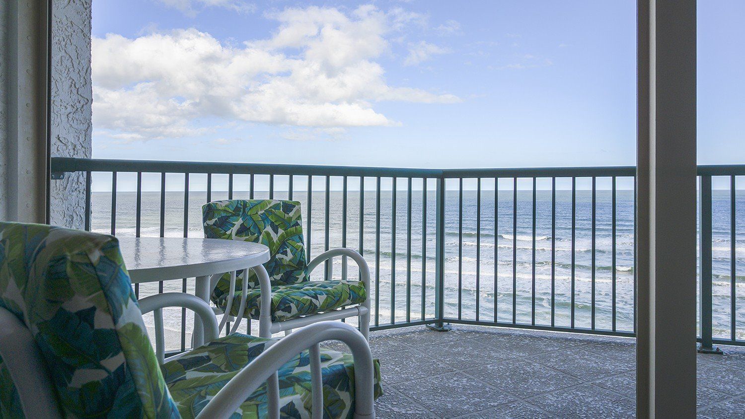 Ein Balkon mit Blick auf das Meer, inklusive Tisch und zwei Stühlen mit gemusterten Kissen.