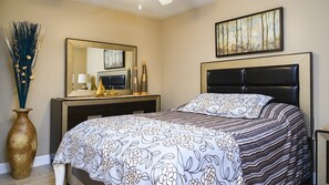 A bedroom with a bed, a dresser, a mirror, a vase, and a painting on the wall.