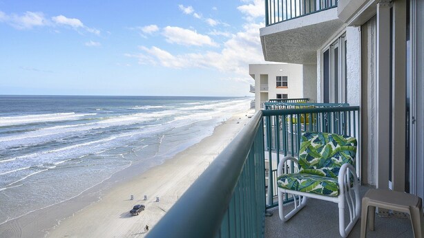 Un balcon avec vue sur la plage et l’océan, une chaise et une petite table.