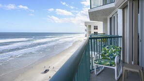 A balcony with a view of the beach and ocean, a chair, and a small table.