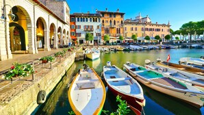 A canal with boats docked, a row of colorful buildings, and a clear blue sky. - Lake Garda Home - 3BR With Balcony Views (Riva del Garda)