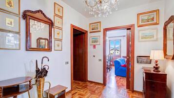 Un pasillo de hotel con suelo de madera, obras enmarcadas en las paredes, un candelabro y vistas a una habitación con sofá azul.