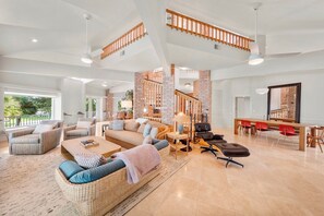 A spacious living area with a high ceiling, a staircase, and a dining area with red chairs. - Ponce Inlet Waterfront Escape - 4 Bedroom 3 Bath (Ponce Inlet)