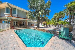 A swimming pool with a clear blue water, surrounded by a paved patio and a house with a covered outdoor area. - Ponce Inlet Waterfront Escape - 4 Bedroom 3 Bath (Ponce Inlet)