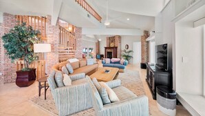 A spacious living area with a large sofa set, a coffee table, and a TV. There is a staircase with wooden railings leading to an upper level. - 151 Bounty LN - Daytona Beach Oceanfront Vacations, Inc (Ponce Inlet)