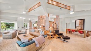 A spacious living area with a high ceiling, a staircase, and a dining area with red chairs. - 151 Bounty LN - Daytona Beach Oceanfront Vacations, Inc (Ponce Inlet)