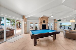 A pool table in a room with a view of the outdoors, a fireplace, and a sofa. - Ponce Inlet Waterfront Escape - 4 Bedroom 3 Bath (Ponce Inlet)