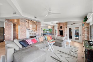 A spacious living room with a sectional sofa, a small white table, and a brick accent wall. - Ponce Inlet Waterfront Escape - 4 Bedroom 3 Bath (Ponce Inlet)