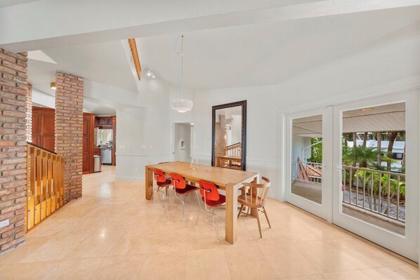 A spacious dining area with a wooden table and red chairs, a brick column, and a view of the outdoors through large sliding glass doors.