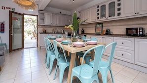 Une cuisine moderne avec des meubles blancs, une table à manger en bois et des chaises de couleur turquoise.