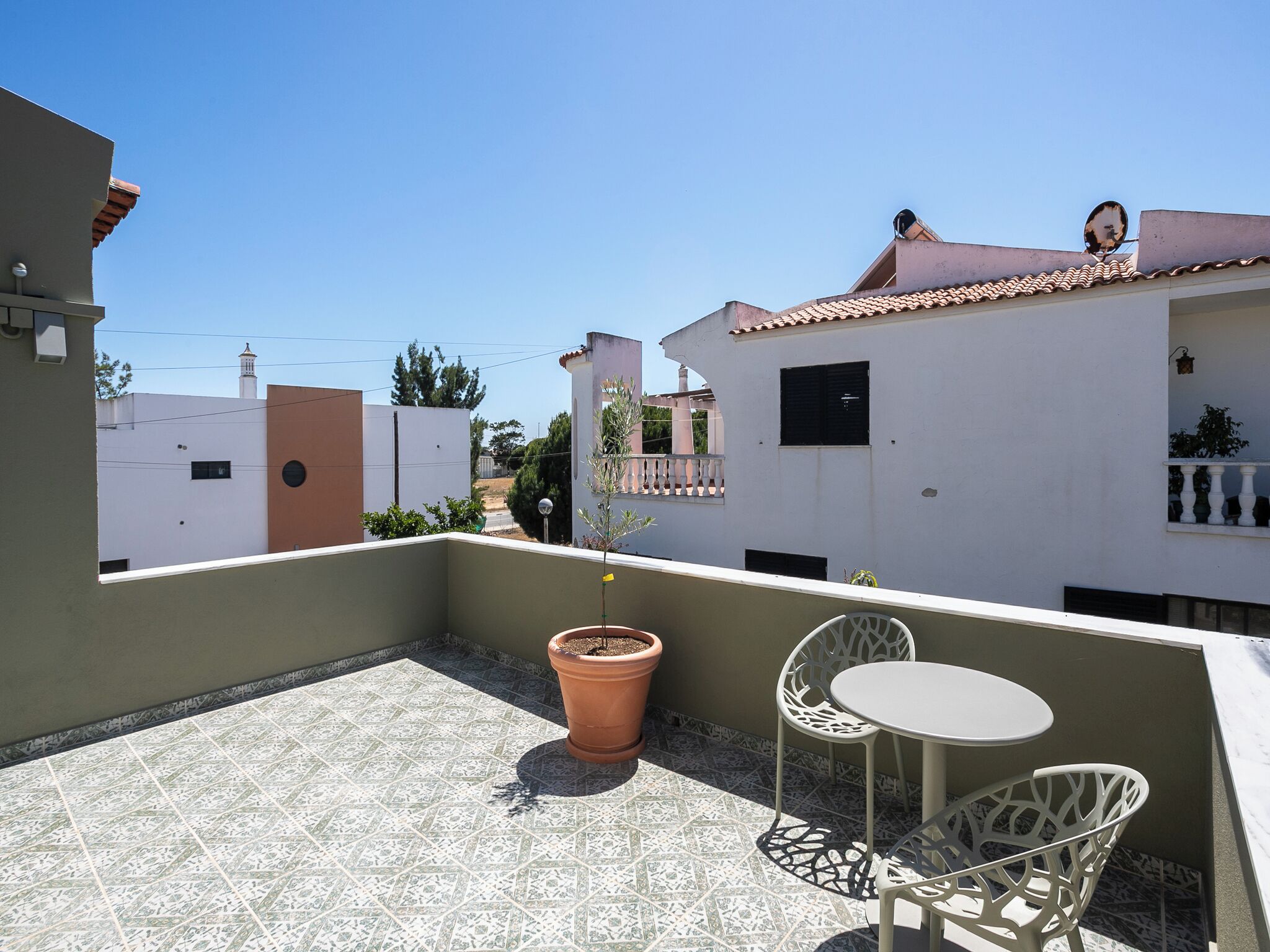 A rooftop terrace with a tiled floor, a potted plant, and a small table with chairs.