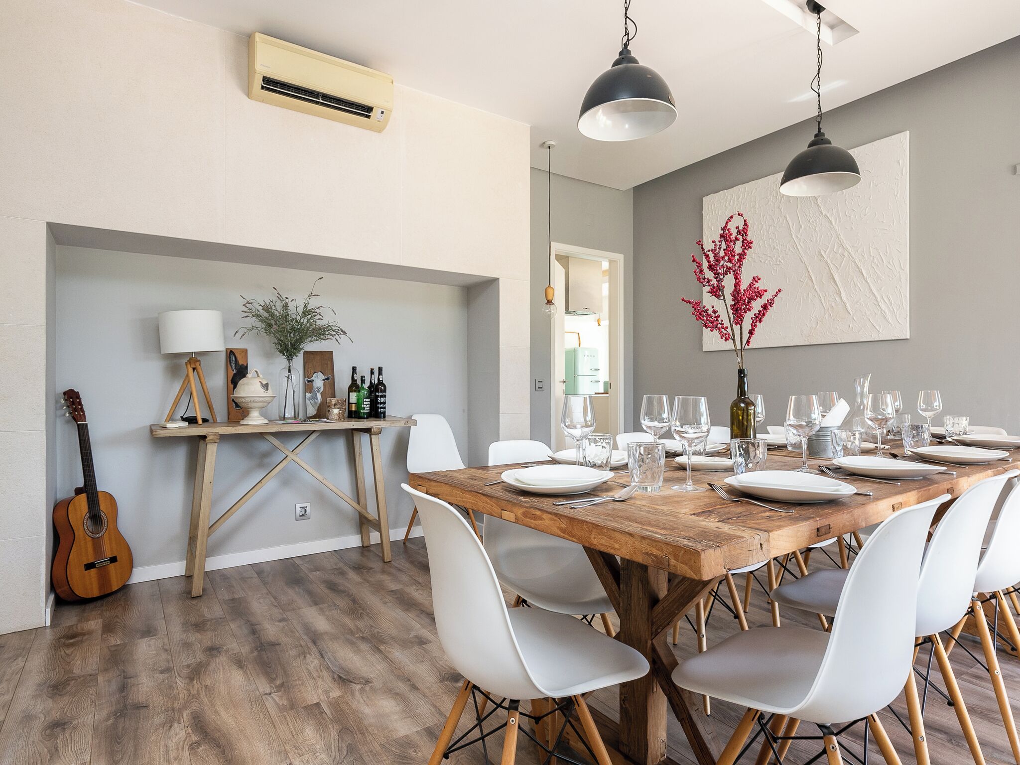 Comedor con mesa de madera dispuesta para seis personas, sillas blancas y una guitarra apoyada contra la pared.