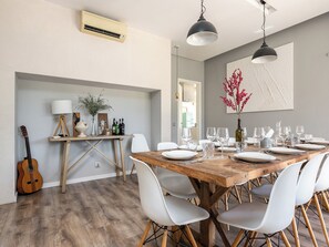 Comedor con mesa de madera dispuesta para seis personas, sillas blancas y una guitarra apoyada contra la pared.