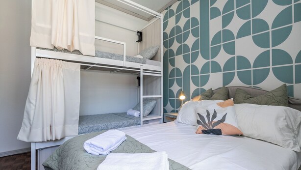 A dorm-style room with bunk beds, a bed with a green quilt, and a patterned wall.