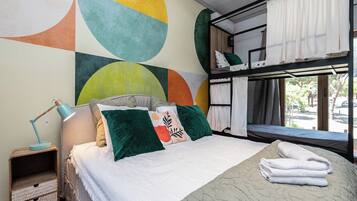 A bedroom with a bunk bed, a bedside table with a lamp, and a large abstract wall mural.