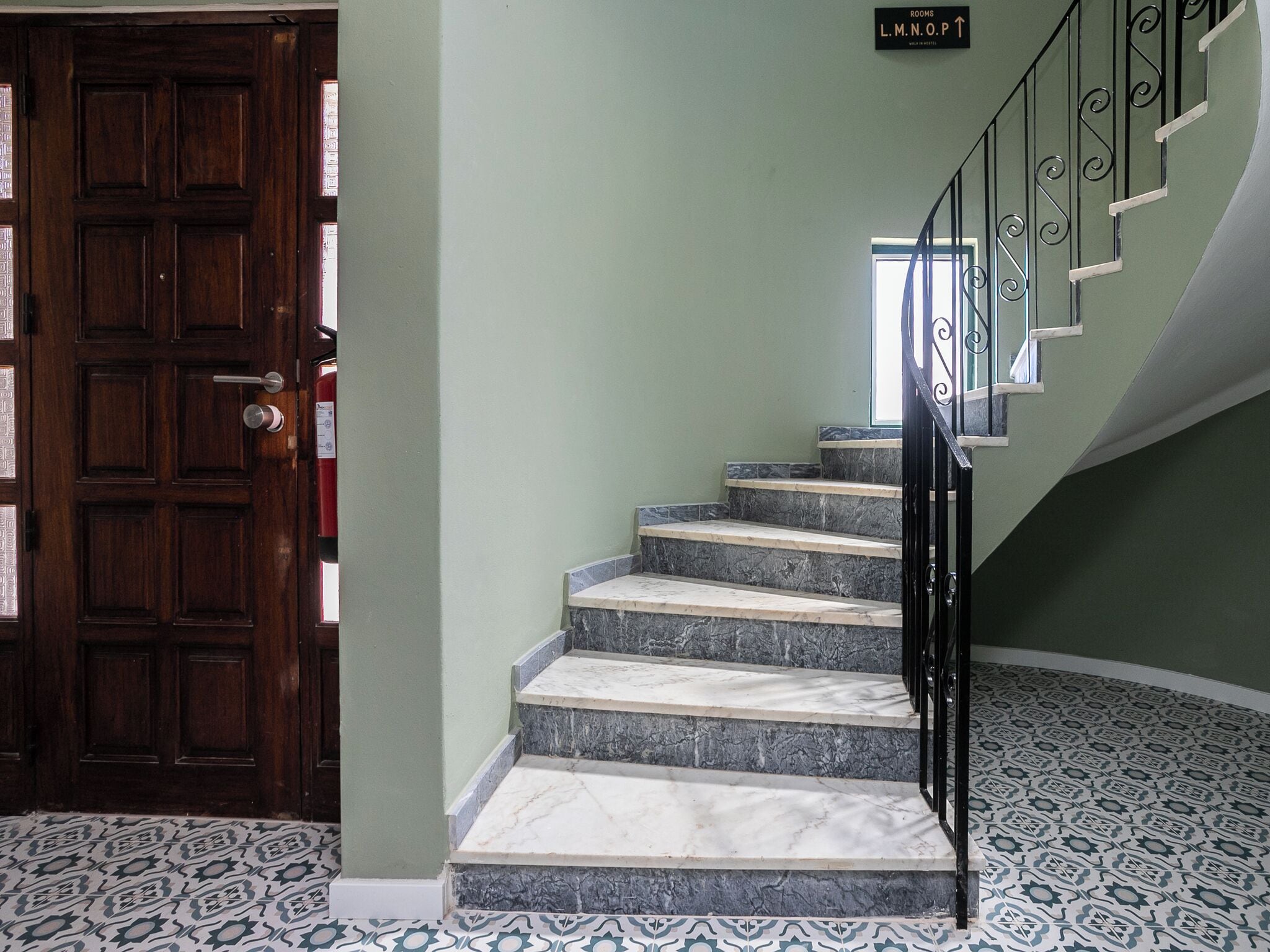 Una escalera con escalones de mármol, una puerta de madera y un letrero que indica 'Rooms L.M.N.O.P.'