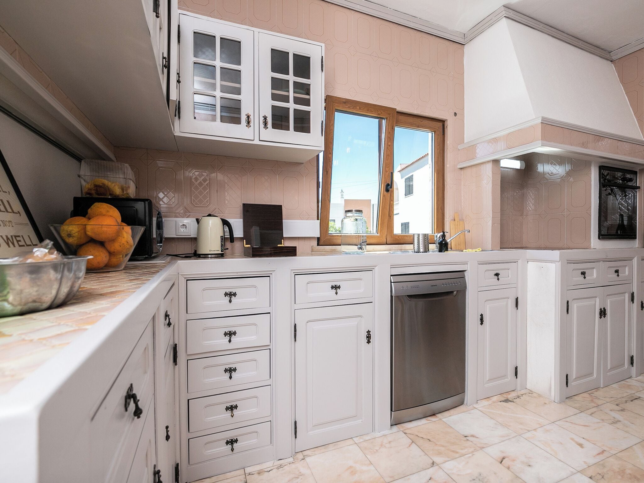 Een keuken met witte kasten, een vaatwasser en een raam met uitzicht op gebouwen.