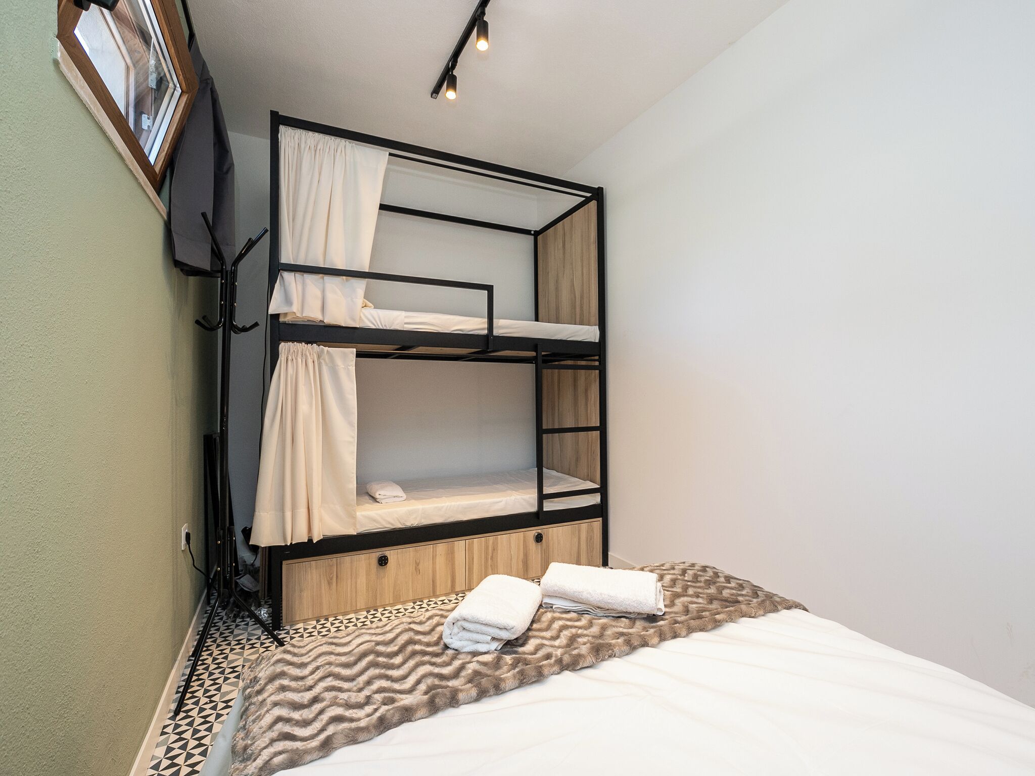 A bunk bed room with a wooden headboard, a patterned rug, and a window with curtains.